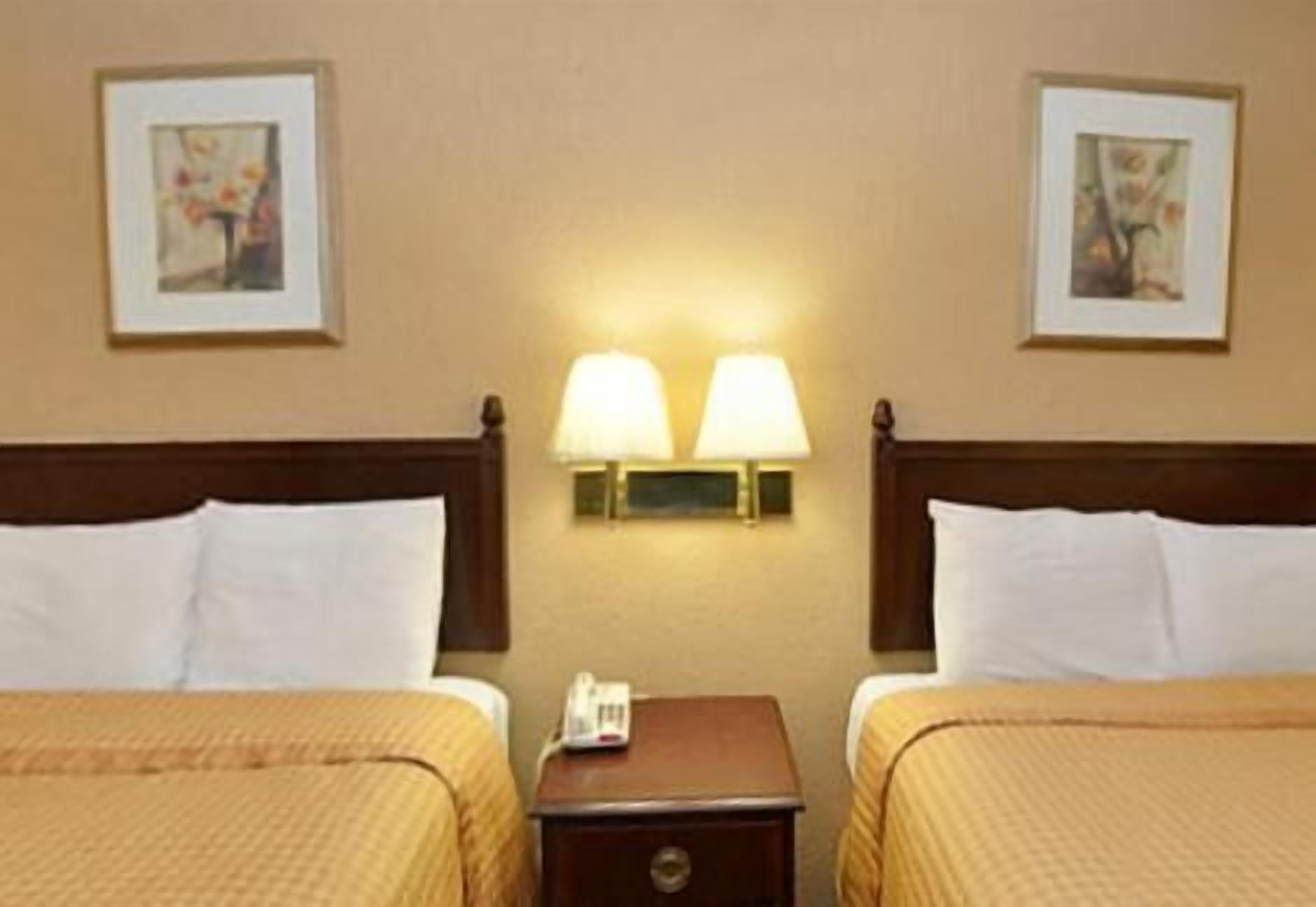 A hotel room with two beds, a nightstand, and wall-mounted lamps.