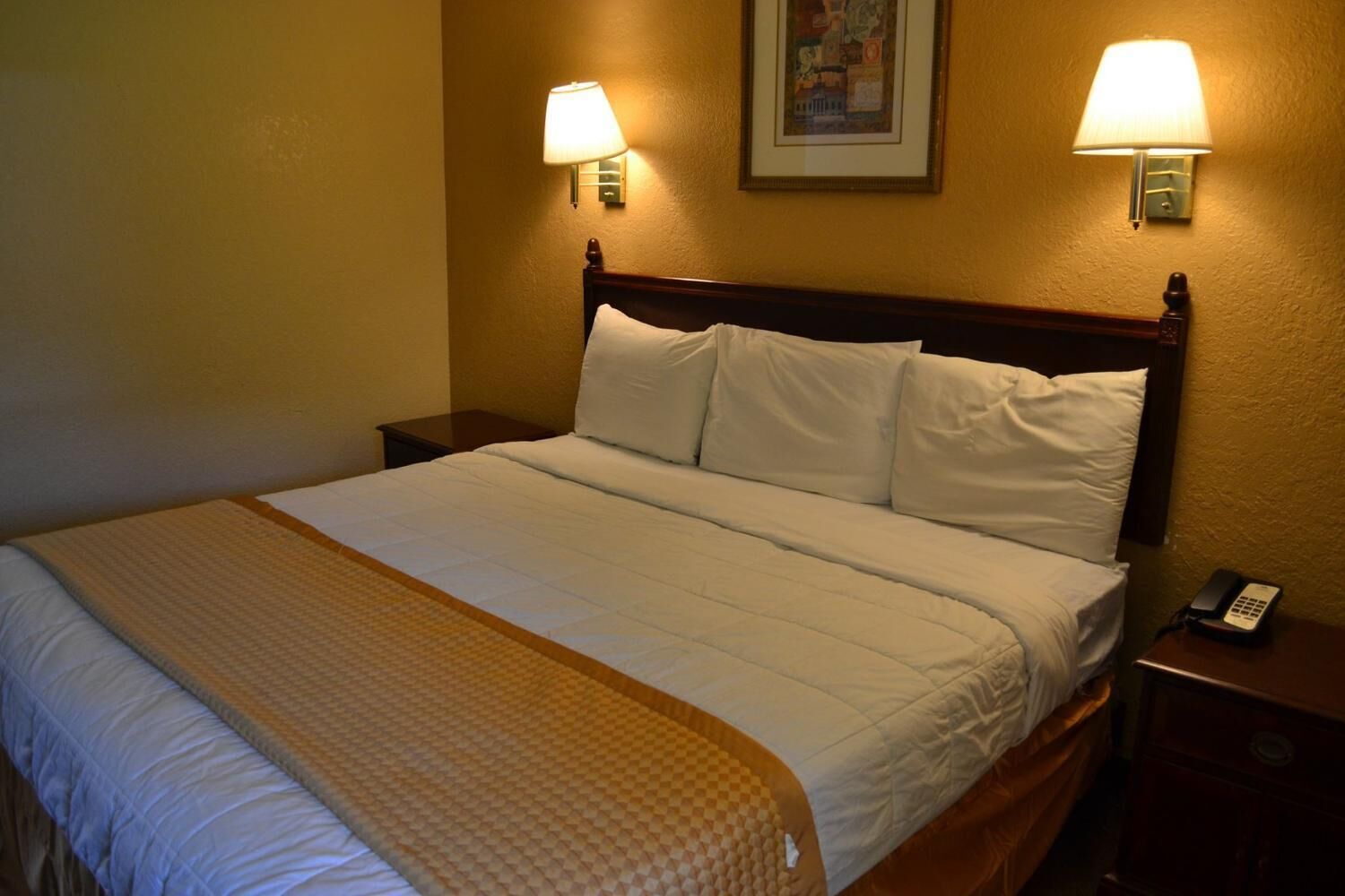 Una cama bien hecha con cabecera de madera, dos lámparas de noche y un teléfono en la mesita.