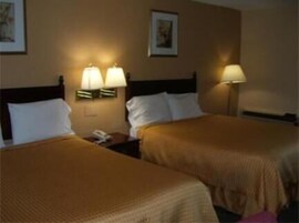 A hotel room with two beds, each with a headboard and a bedside table. There are wall-mounted lamps on either side of the beds.