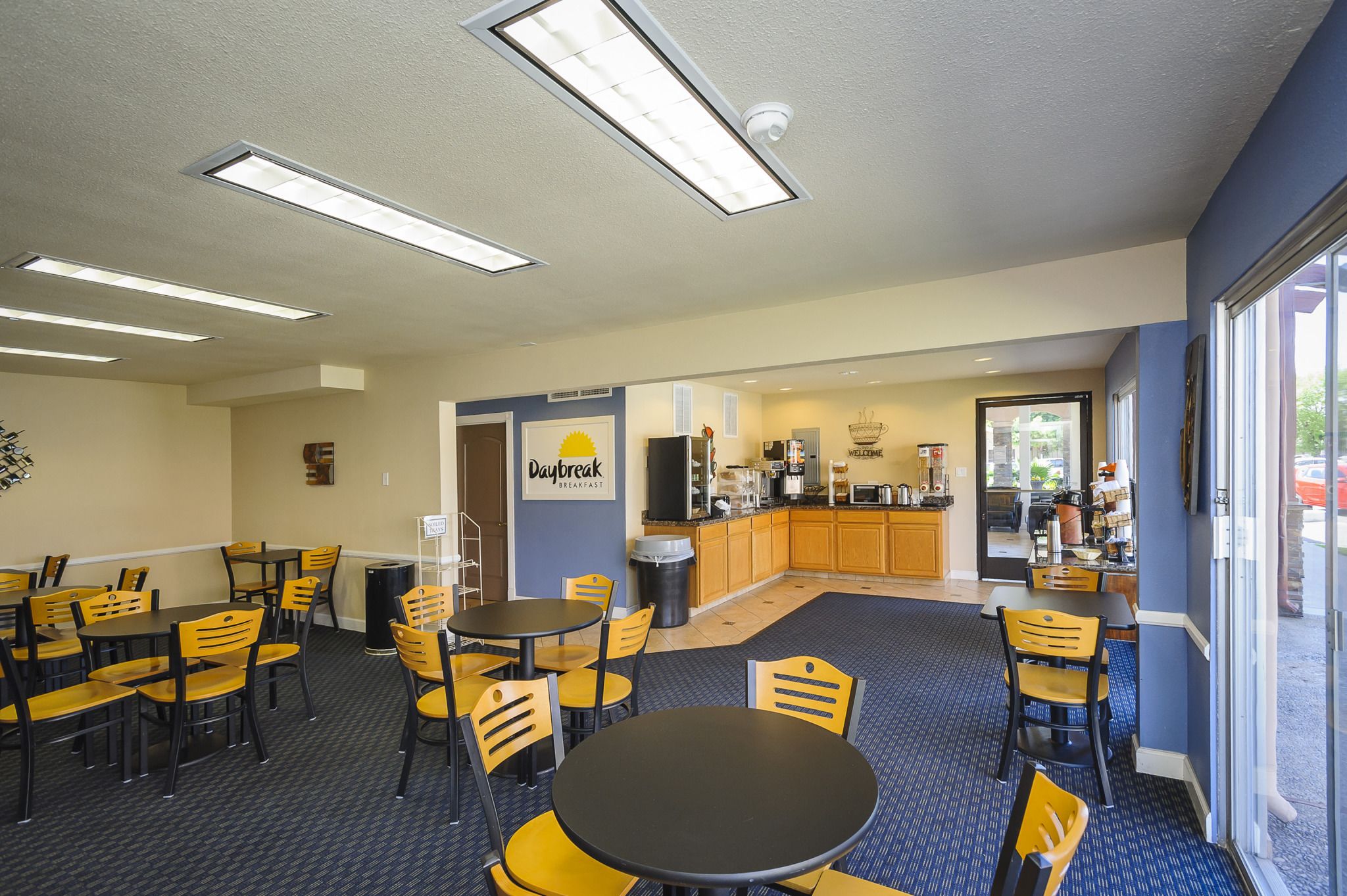 A breakfast area with tables and chairs, a kitchen in the background, and a sign that reads "Daybreak Breakfast".