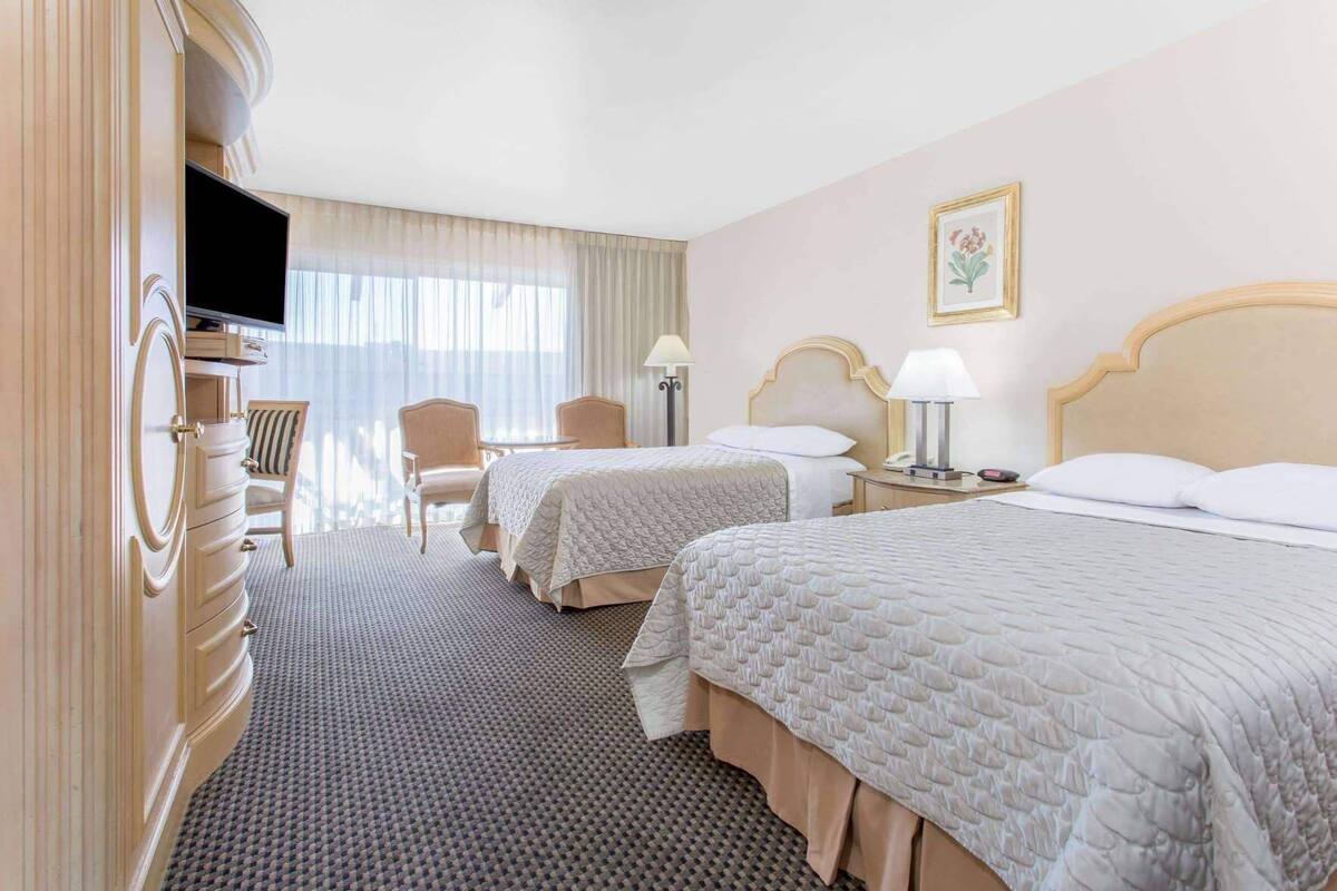 A hotel room with two beds, a TV, a desk, a chair, and a window with curtains.