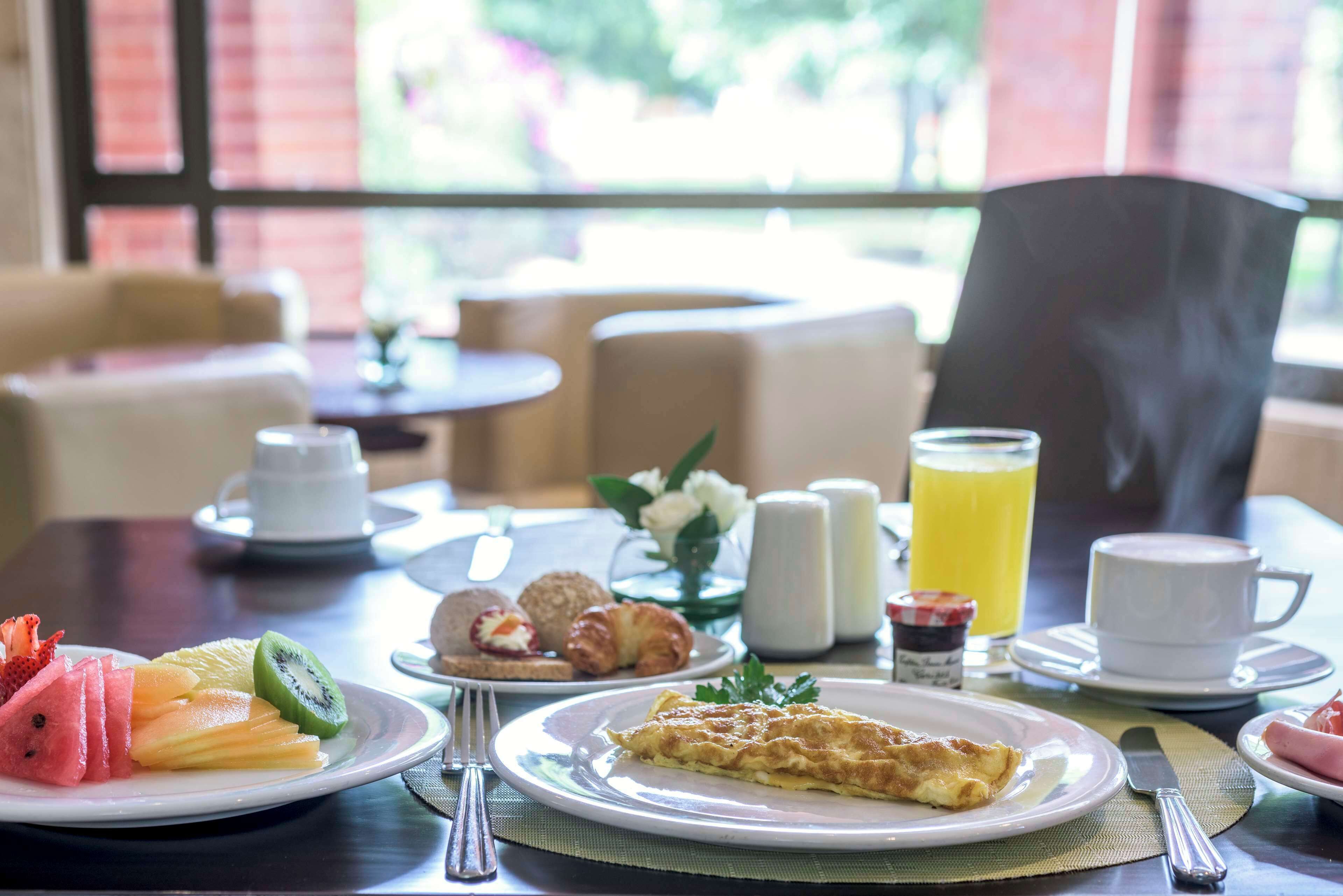 A breakfast setting with plates of fruit, croissants, and an omelette, along with cups of coffee and a glass of orange juice.