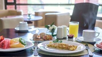 A breakfast setting with plates of fruit, croissants, and an omelette, along with cups of coffee and a glass of orange juice.