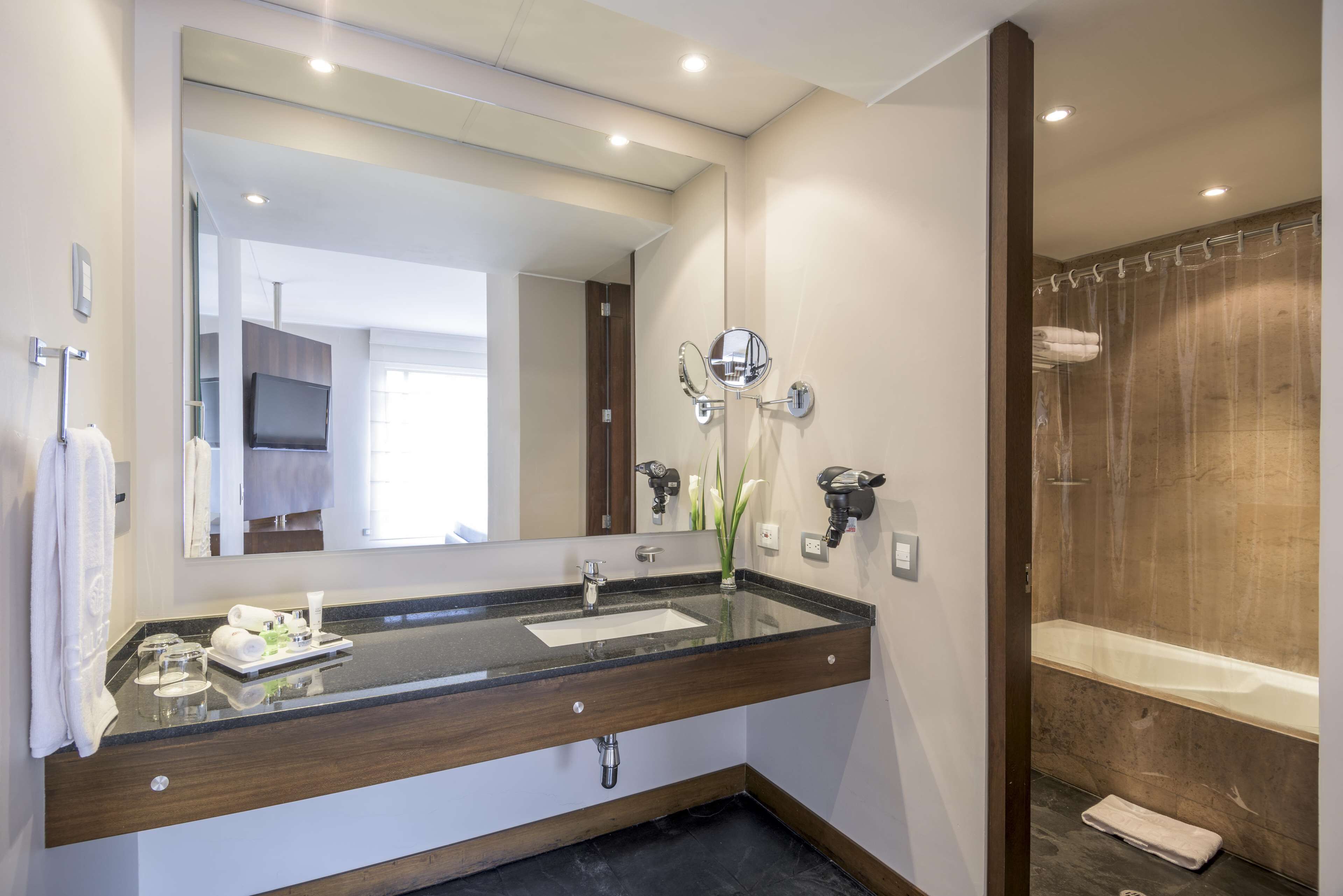 Un baño moderno con un espejo grande, un lavamanos con toallero y una zona de ducha.