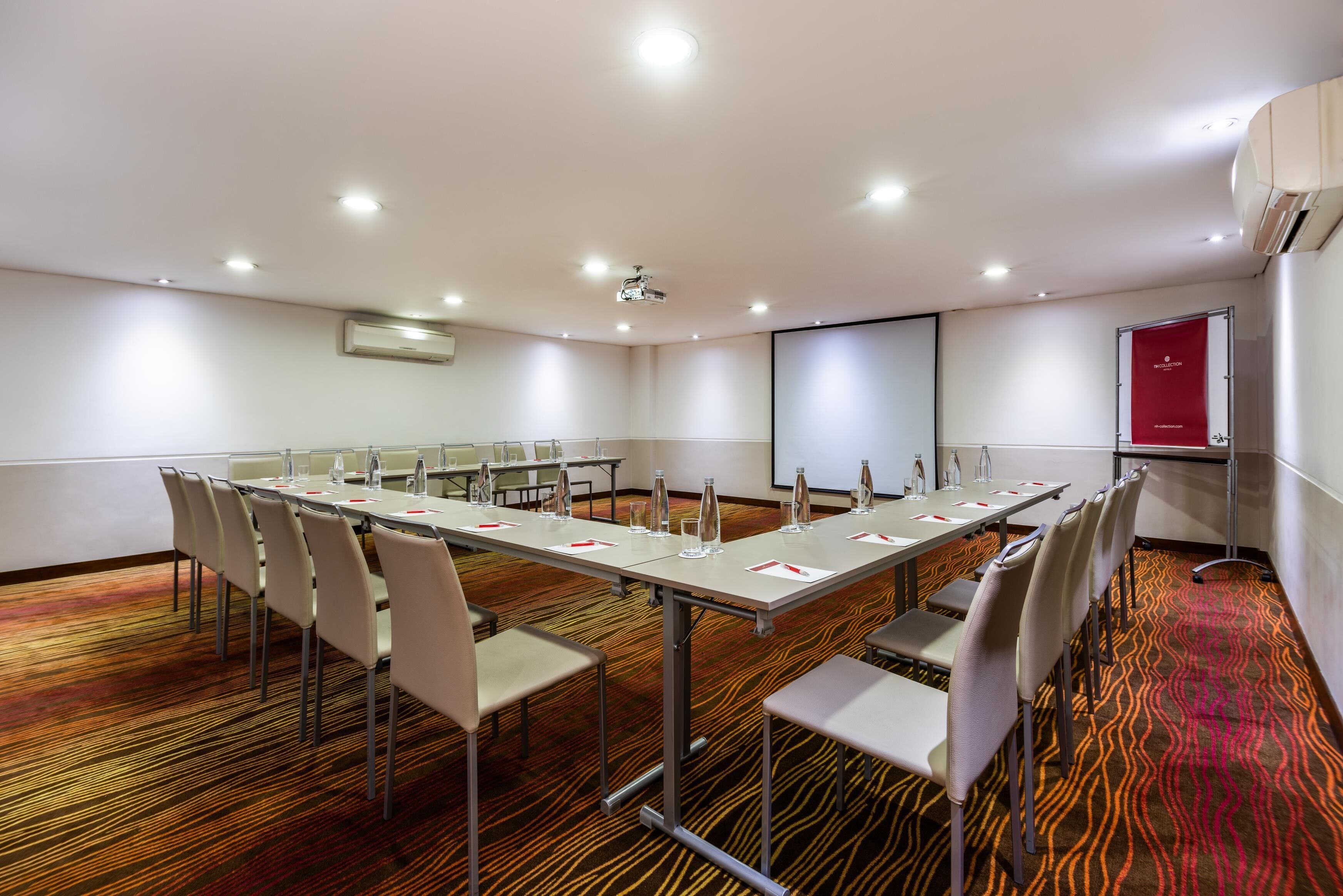 A conference room with a long table, chairs, a projector, and a screen.
