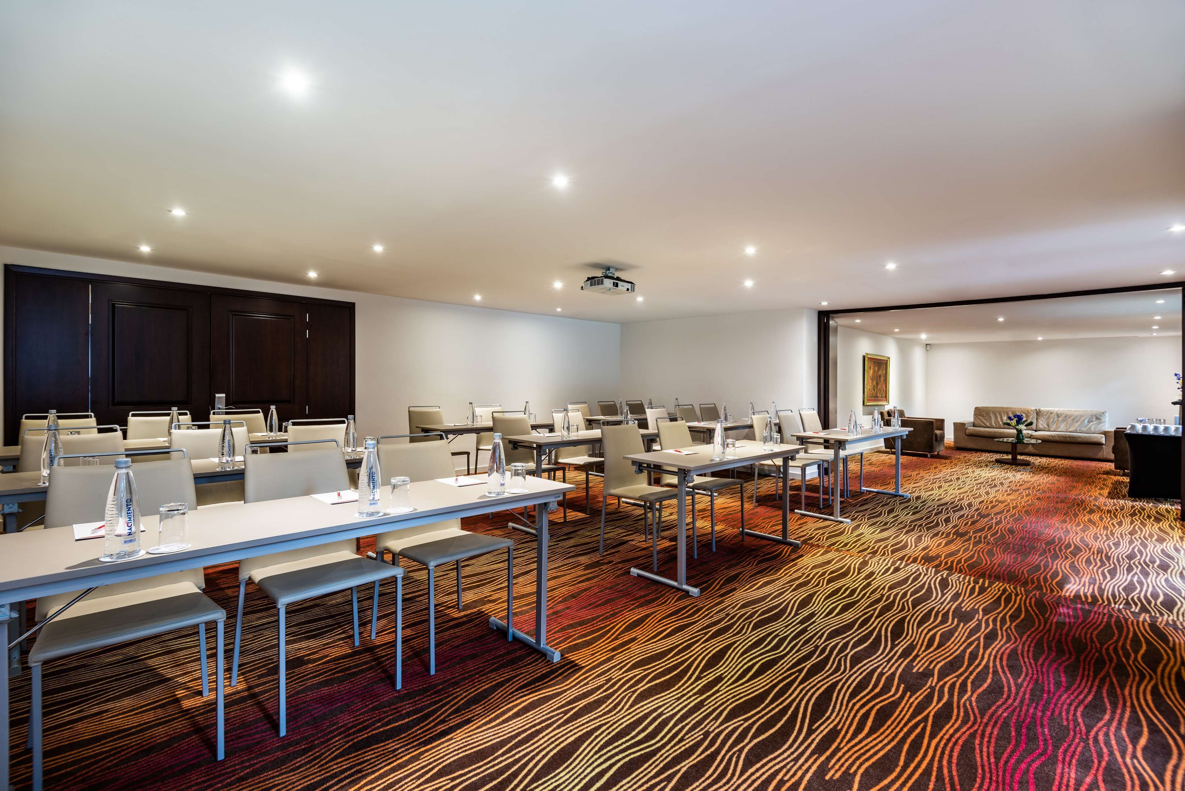 A conference room with multiple tables and chairs, a projector, and a patterned carpet.