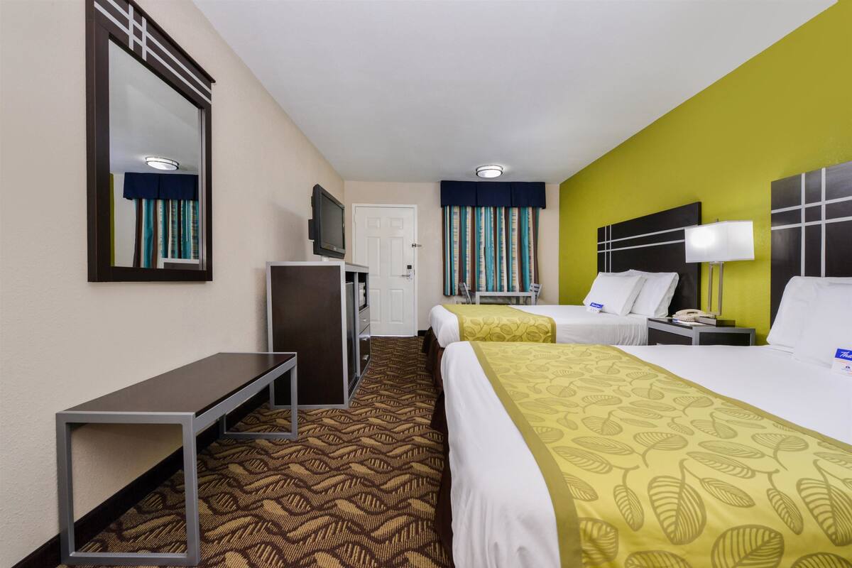 Ein Hotelzimmer mit zwei Betten, einem Schreibtisch, einem Fernseher und einem Spiegel.