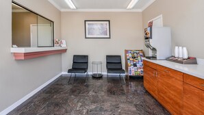 A reception area with a counter, two chairs, a small table, a refrigerator, and a magazine rack. - Americas Best Value Inn Pasadena Houston (Pasadena)