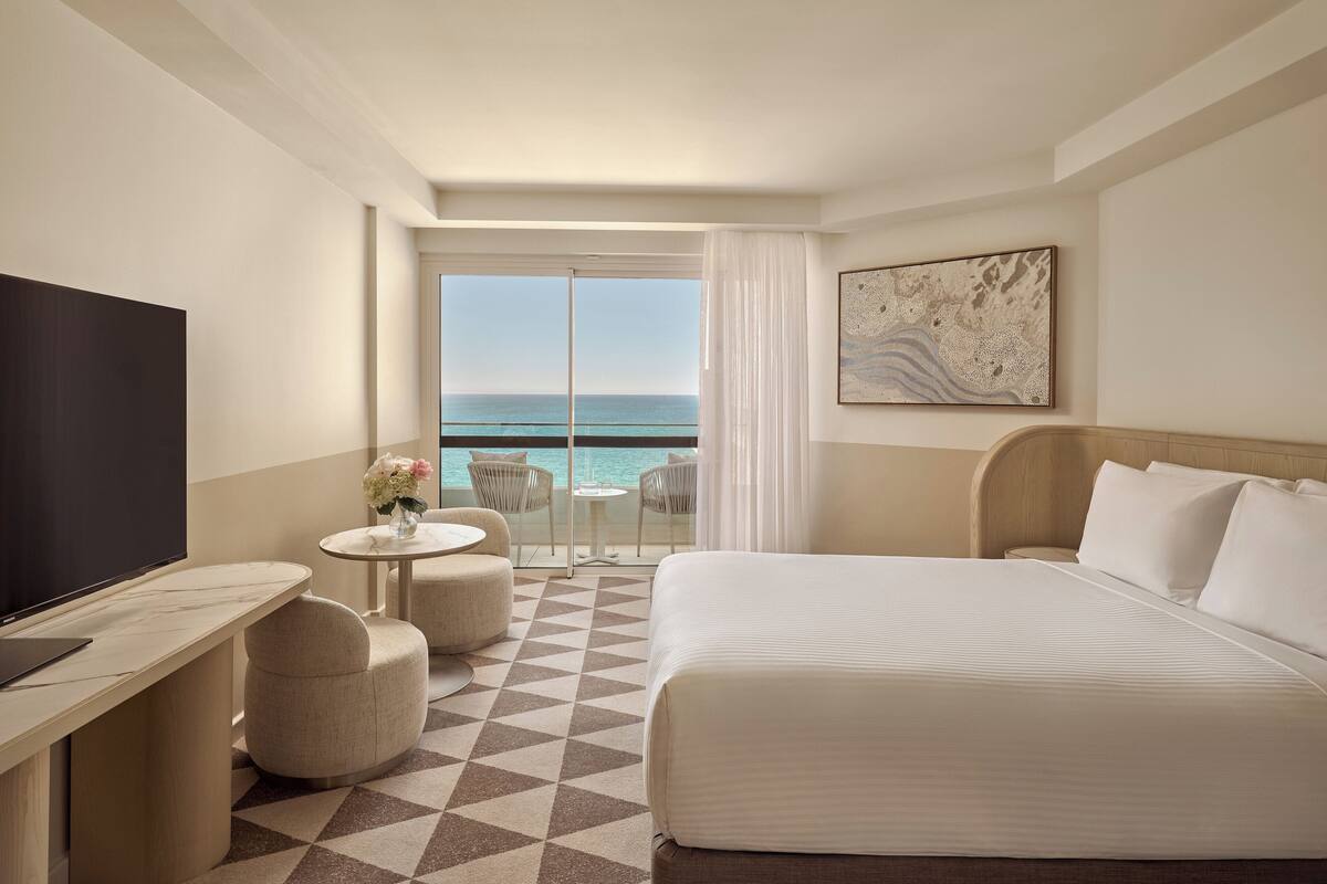 Habitación de hotel con cama, televisión, escritorio y vistas al océano.