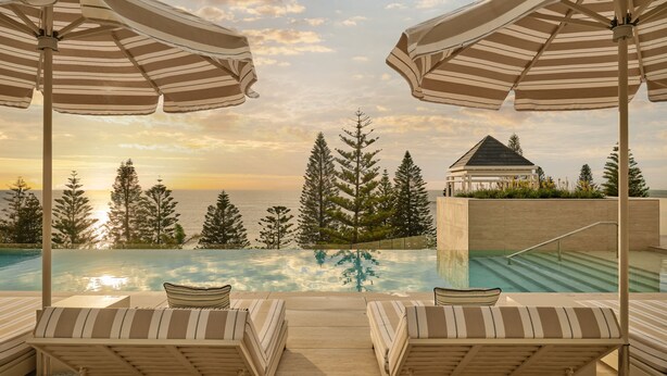 A poolside area with lounge chairs and umbrellas, overlooking a body of water and trees.
