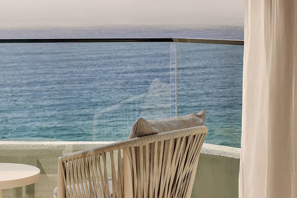 Un balcón con vista al mar, una silla de mimbre y una pequeña mesa redonda.