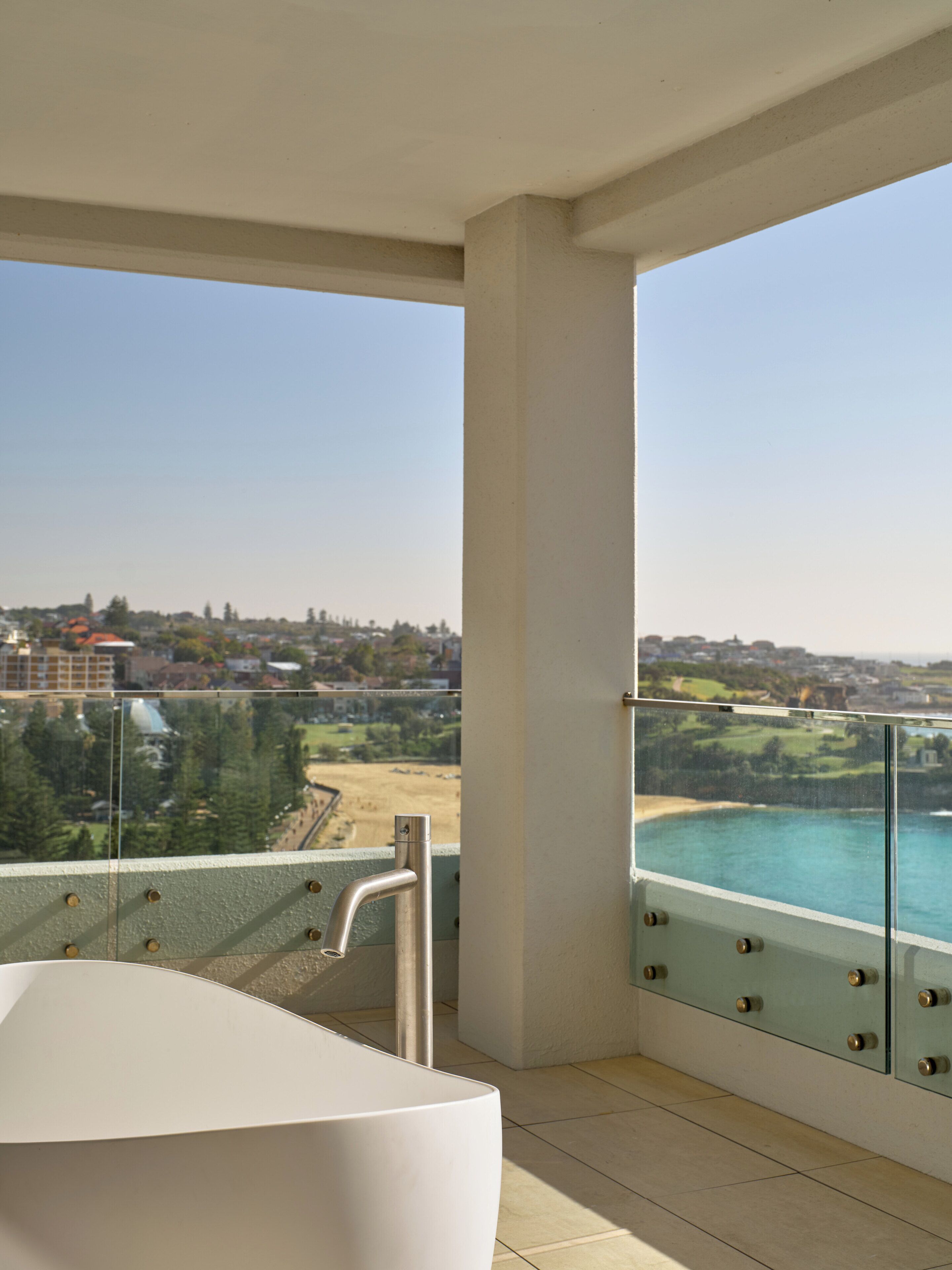 A balcony with a glass railing overlooking a beach and a body of water.