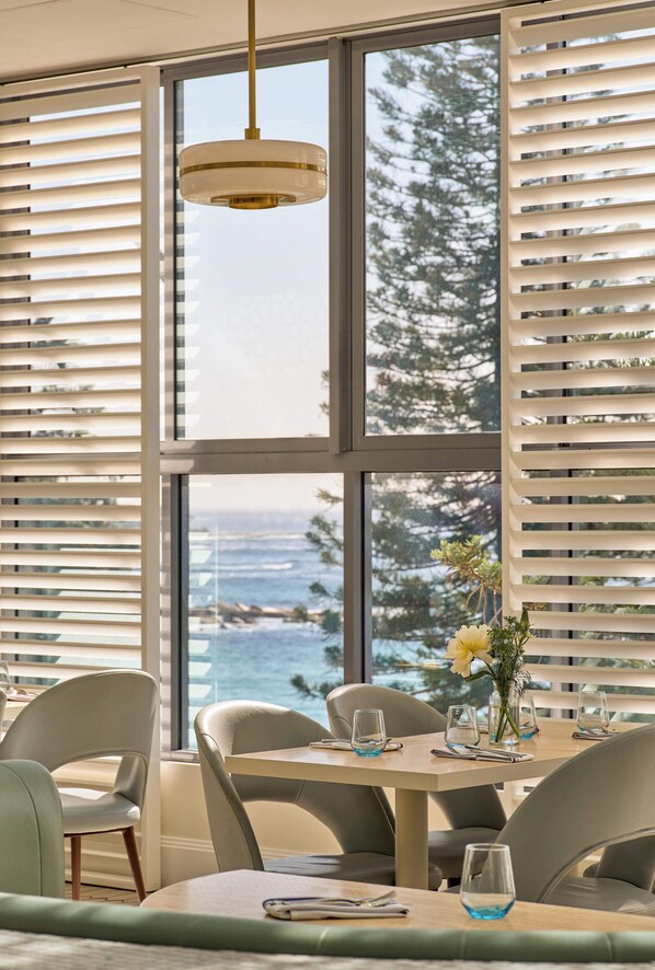 A dining area with a table set for four, large windows with blinds, and a view of the ocean. - InterContinental Sydney Coogee Beach by IHG (Coogee)