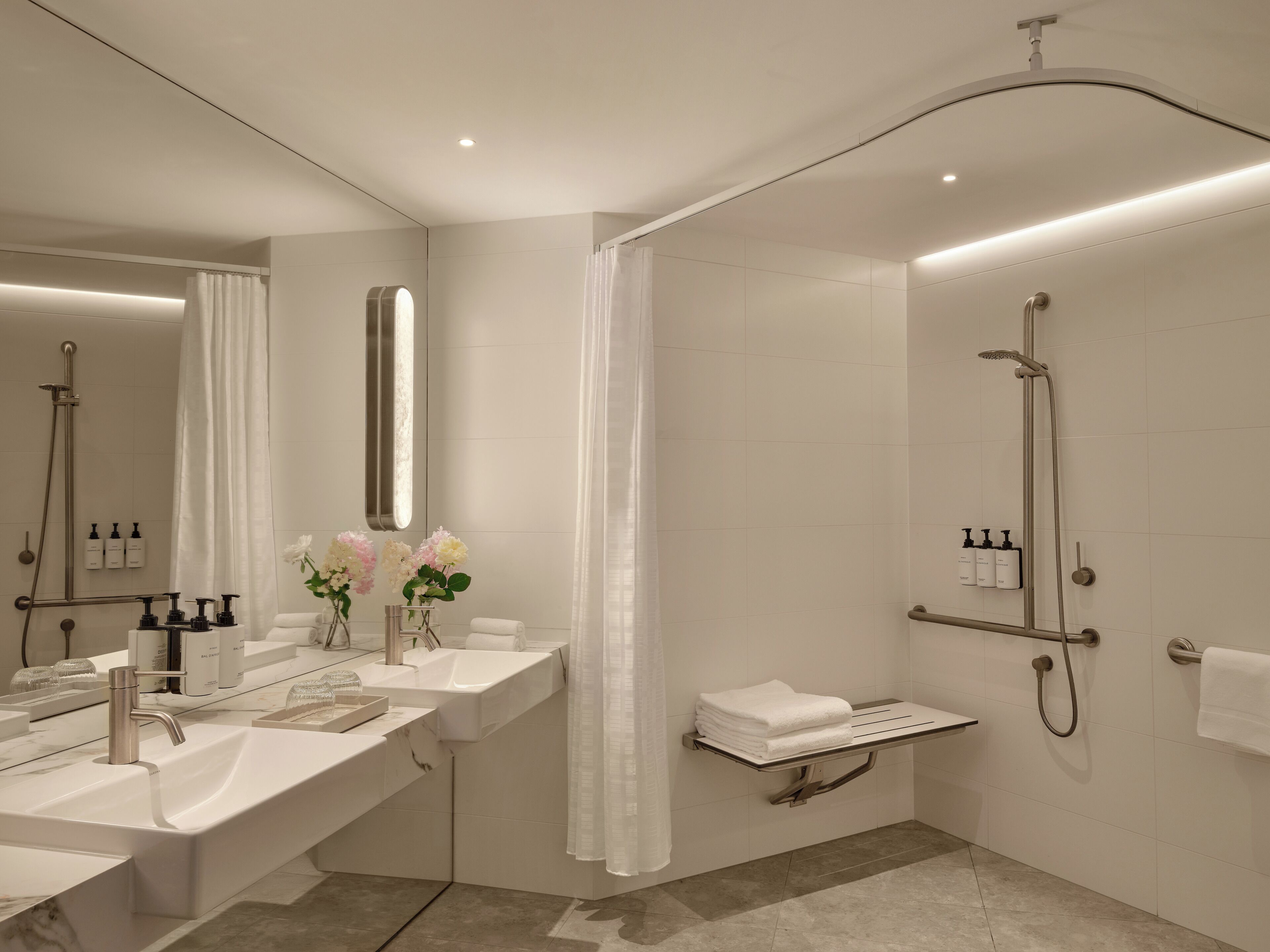 Un bagno moderno con un ampio specchio, due lavandini, una doccia e un portasciugamani.