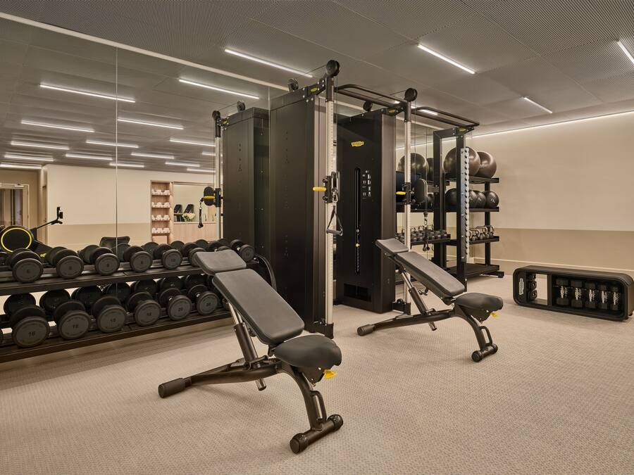 Un gimnasio con equipo de levantamiento de pesas, bancos y mancuernas.