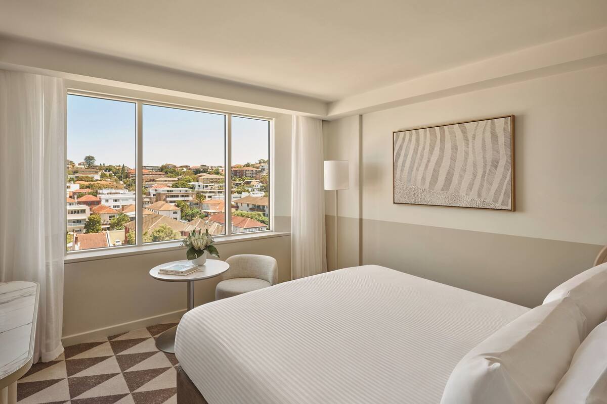 Una habitación de hotel con una cama grande, una mesa redonda pequeña, una silla y una ventana con vistas a la ciudad.