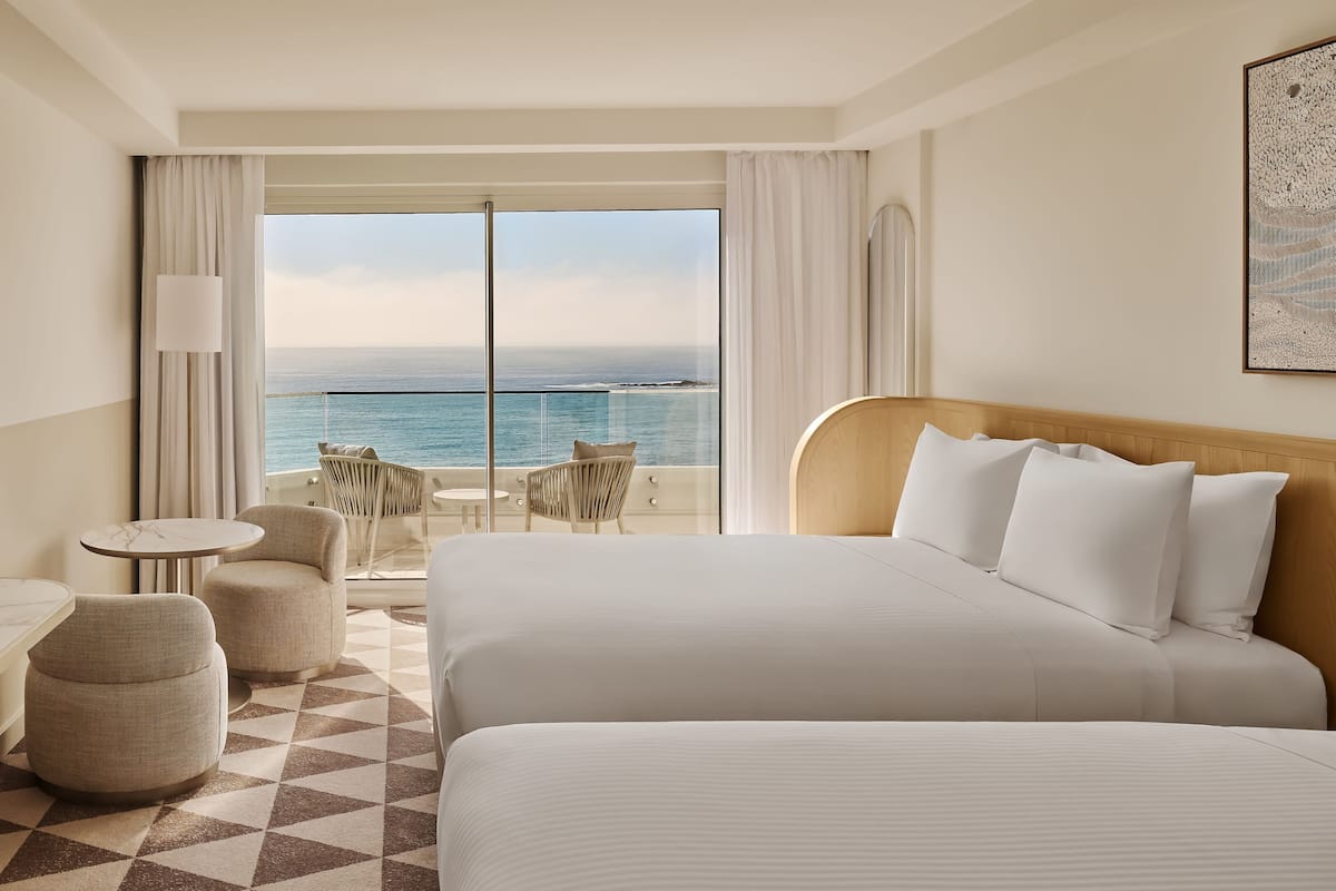 Habitación de hotel con una cama grande, televisión, una mesita y balcón con vistas al mar.
