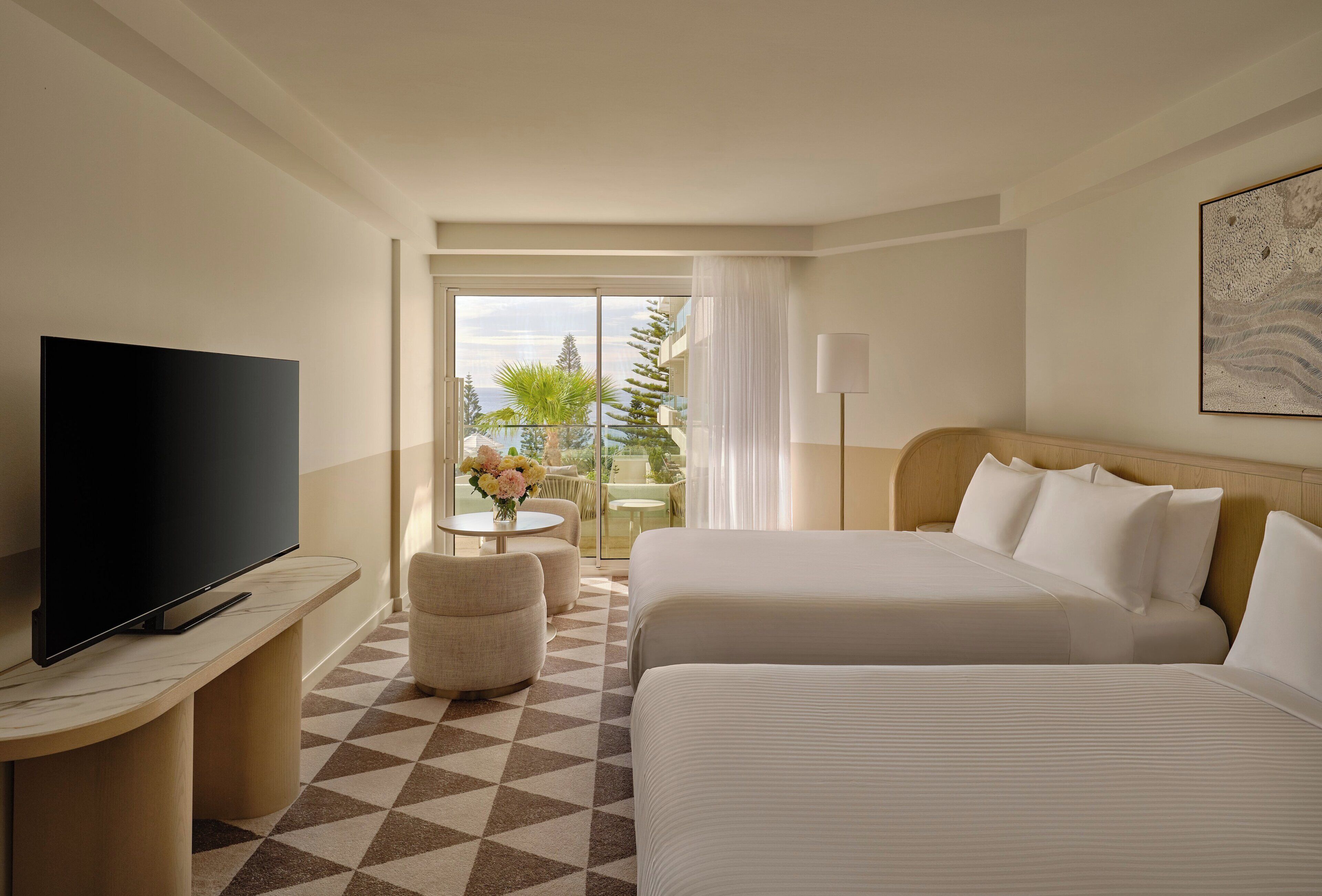 Een hotelkamer met twee bedden, een televisie, een tafeltje met bloemen en een balkon met tuinmeubilair.