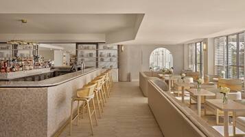 A modern bar area with a long counter, multiple stools, and a seating area with tables and chairs.