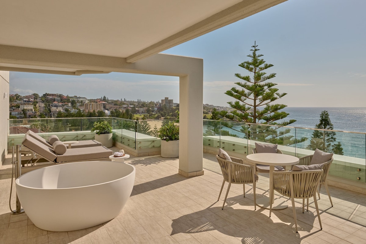 Une terrasse sur le toit avec une grande baignoire blanche, des chaises longues et une table à manger.