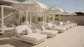 A row of sun loungers with striped cushions, white umbrellas, and potted plants.