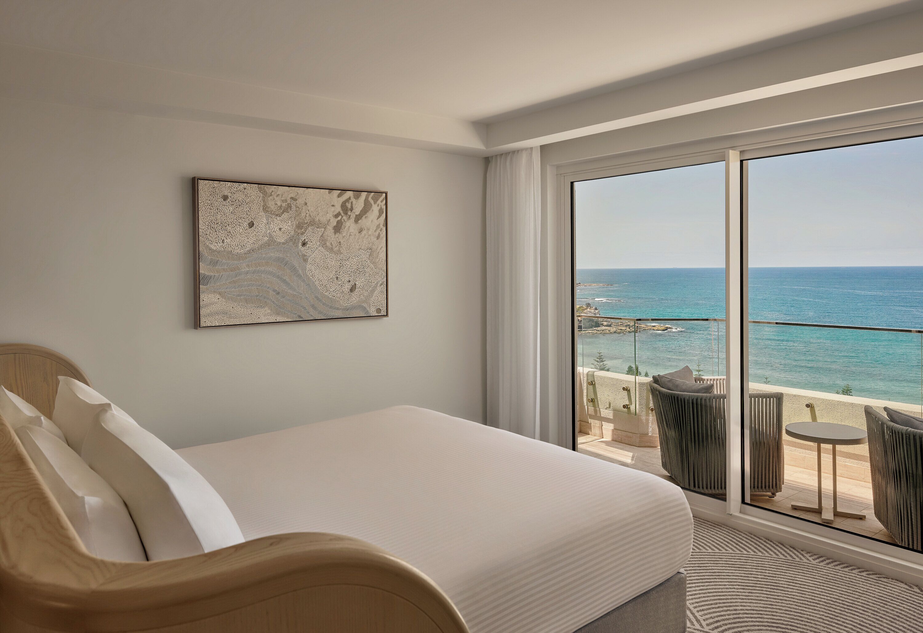 A hotel room with a large bed, a view of the sea, and a balcony with outdoor seating.