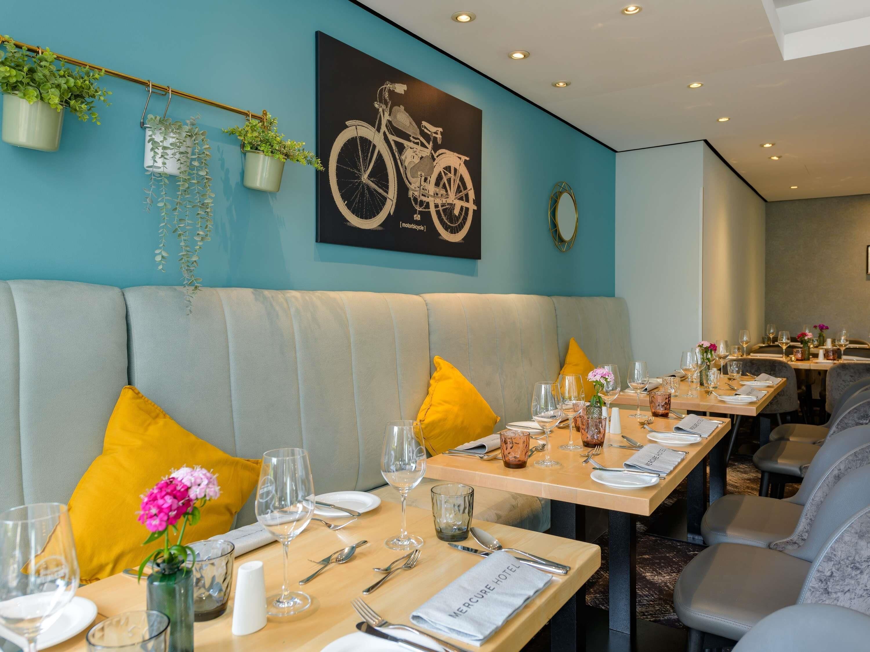 A restaurant with a teal wall, a bicycle artwork, and a seating area with yellow cushions.