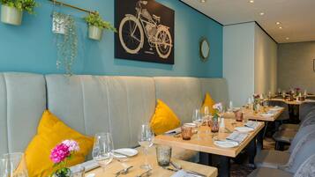 A restaurant with a teal wall, a bicycle artwork, and a seating area with yellow cushions.