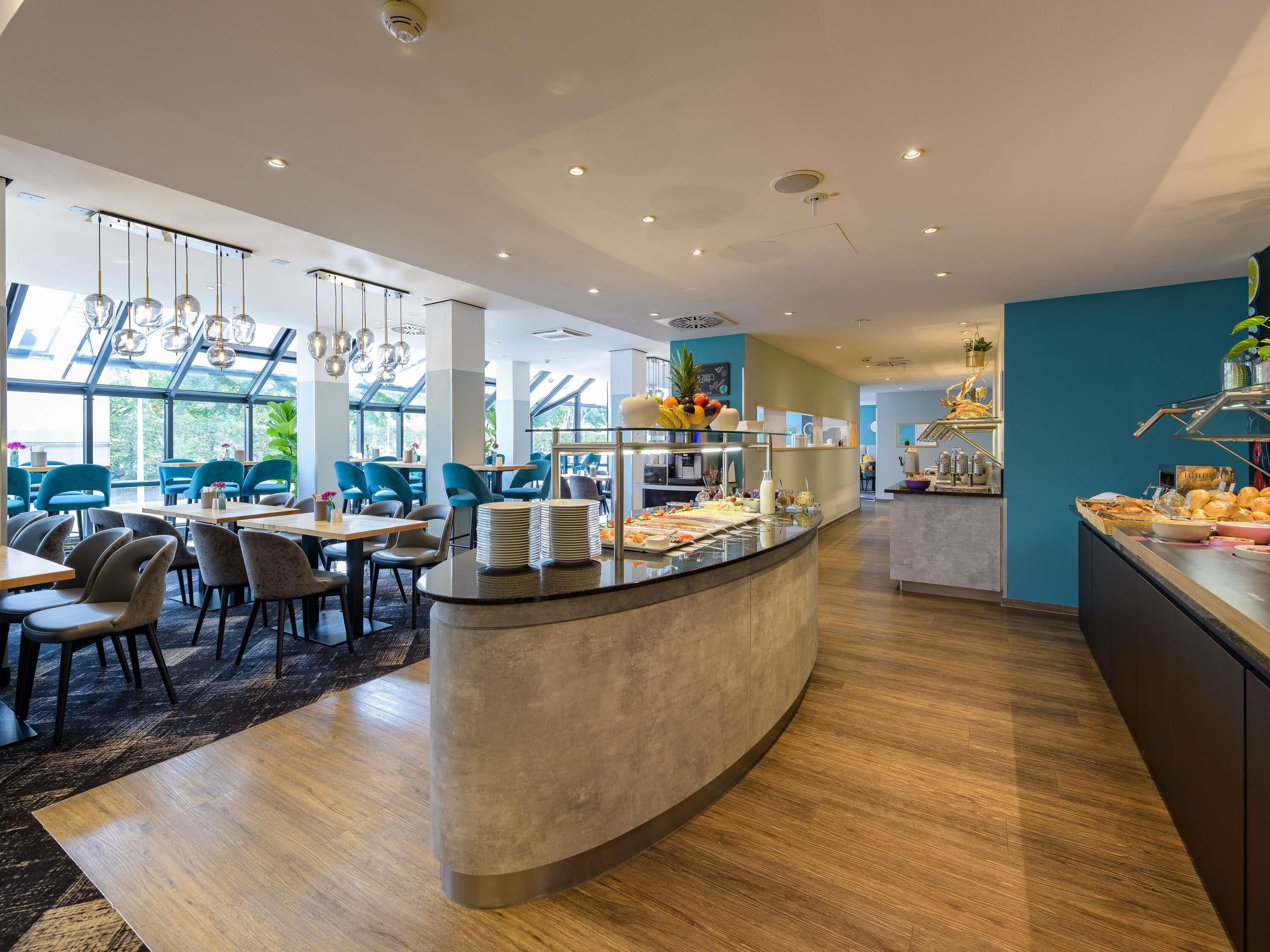 A modern restaurant with a curved counter, blue chairs, and a buffet area.