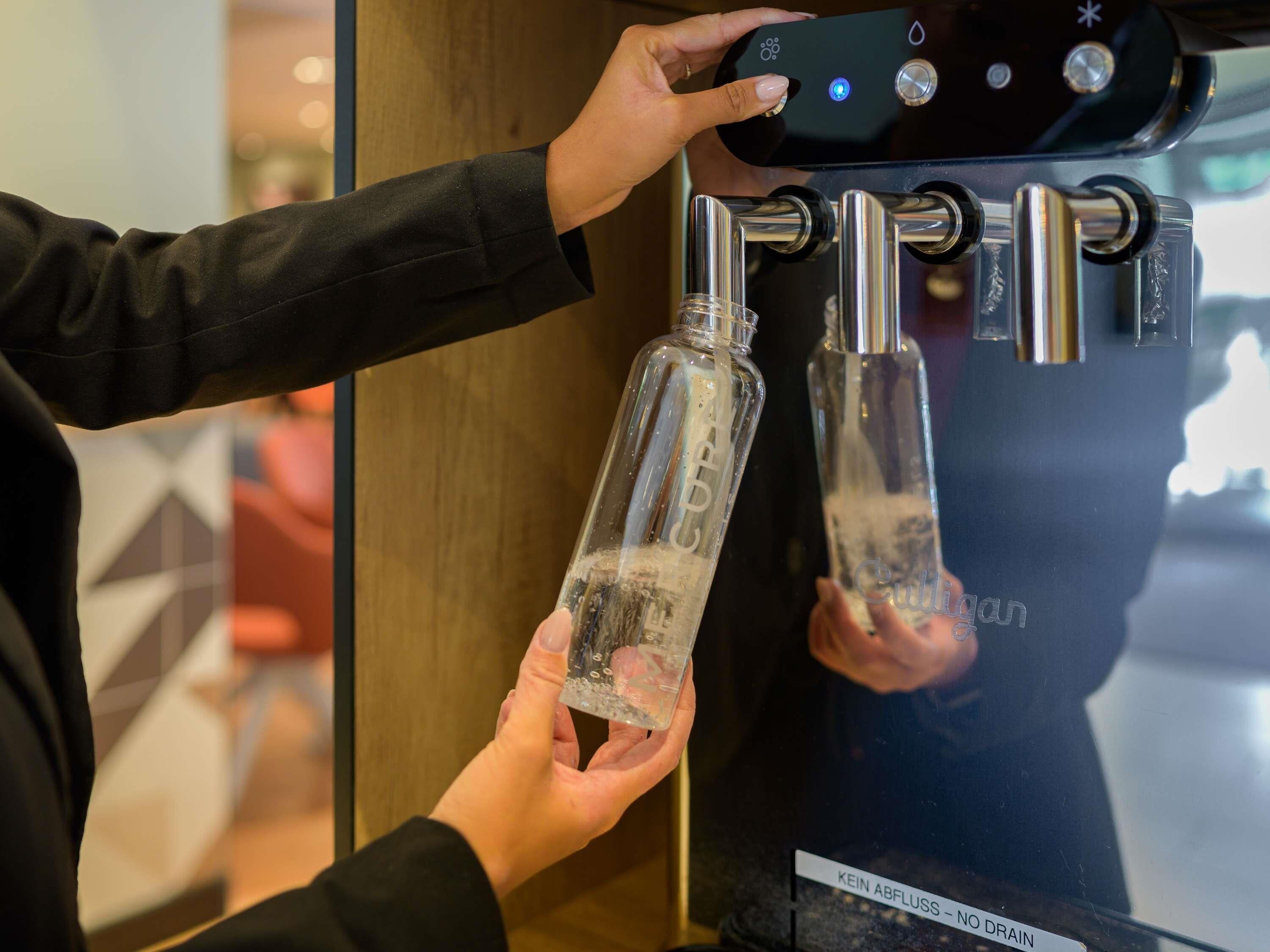 Una persona usando un dispensador de agua con dos grifos, cada uno con una botella.