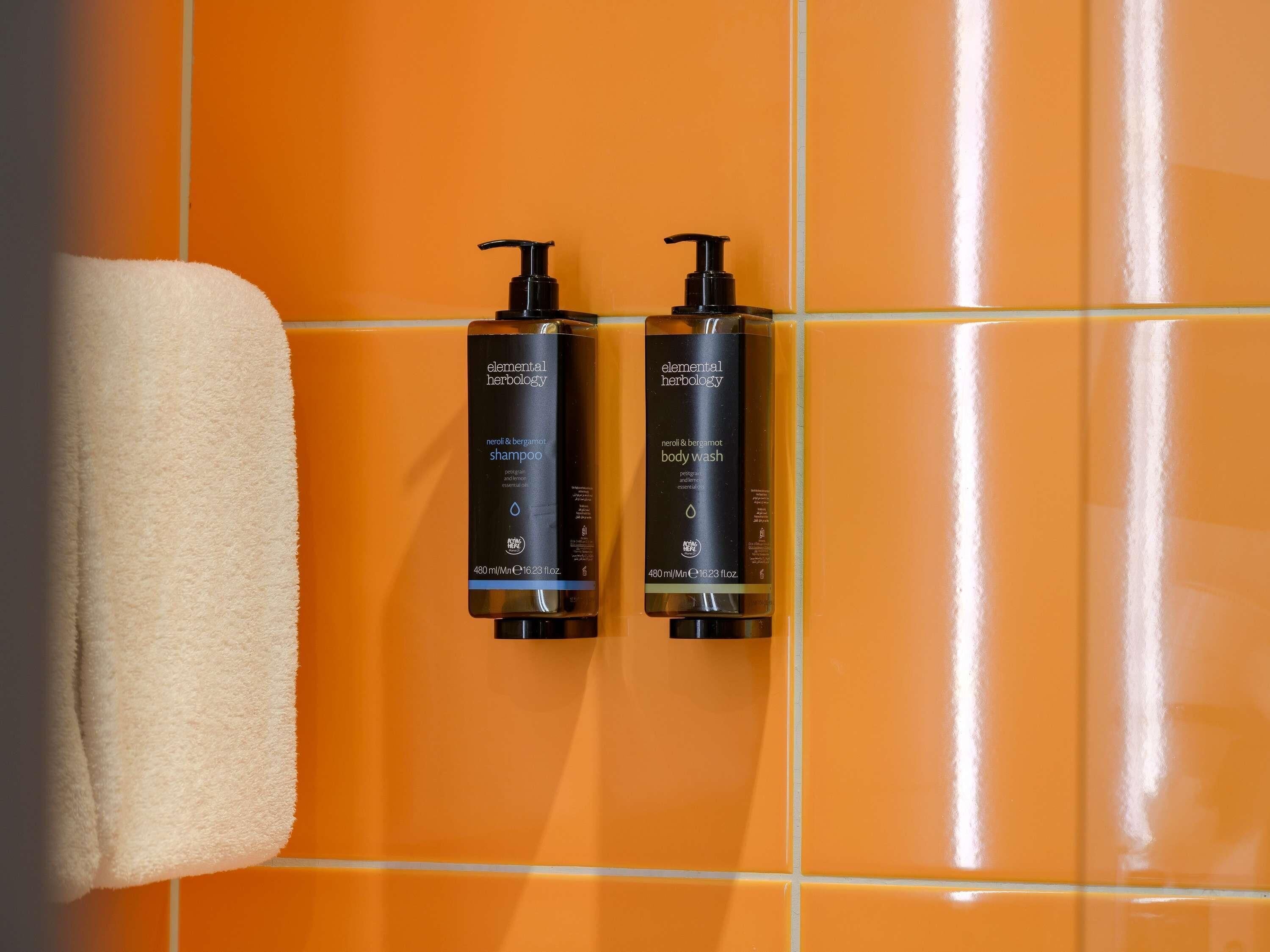 Two bottles of Elemental Herbology shampoo and body wash on a tiled wall.