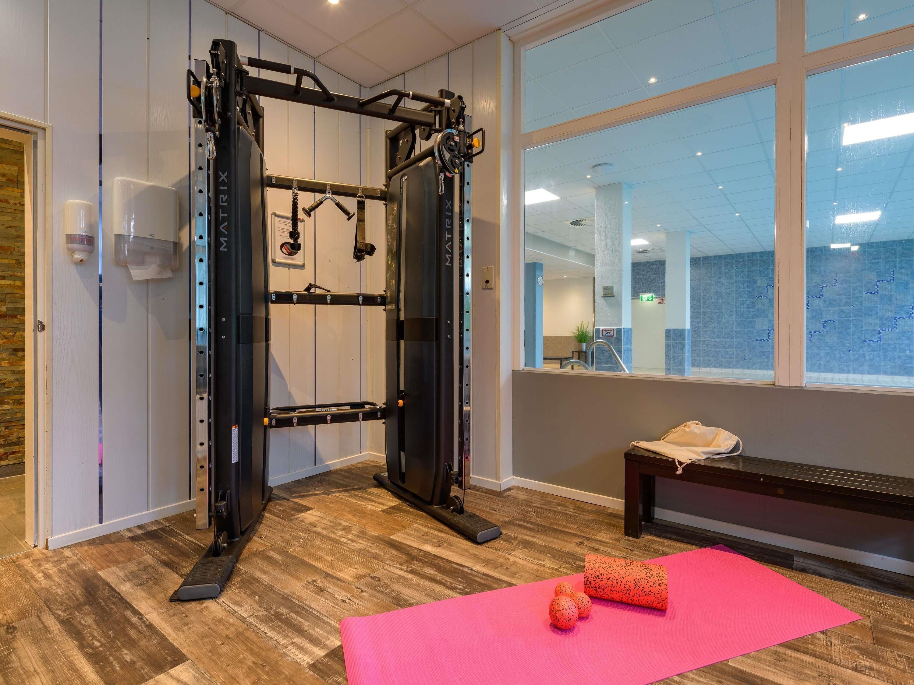 Een sportschool met een optrekstang, een bank en trainingsballen op een roze mat.