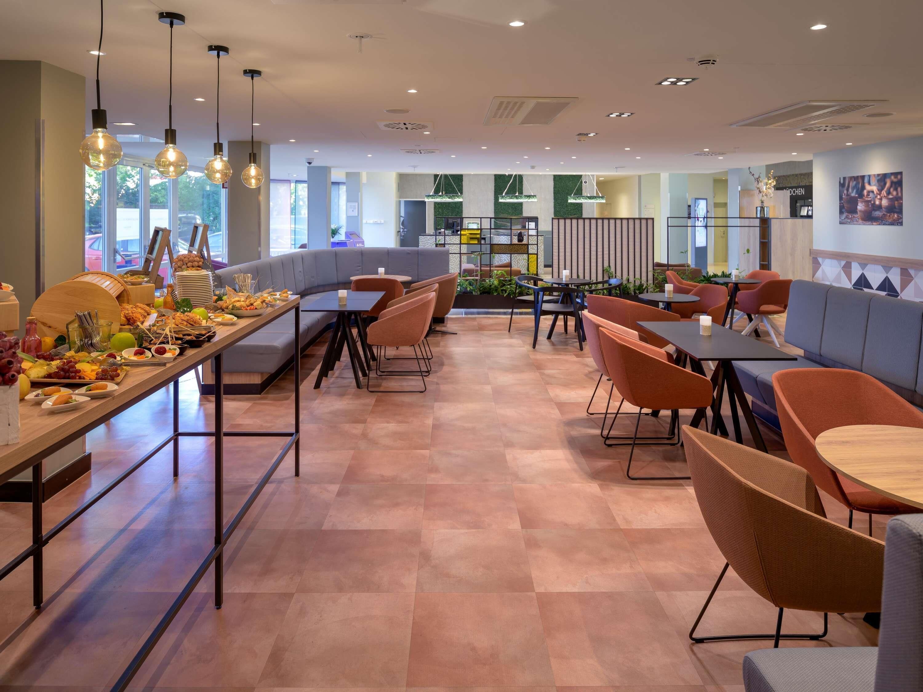 A modern dining area with a long communal table, cushioned seating, and pendant lighting.