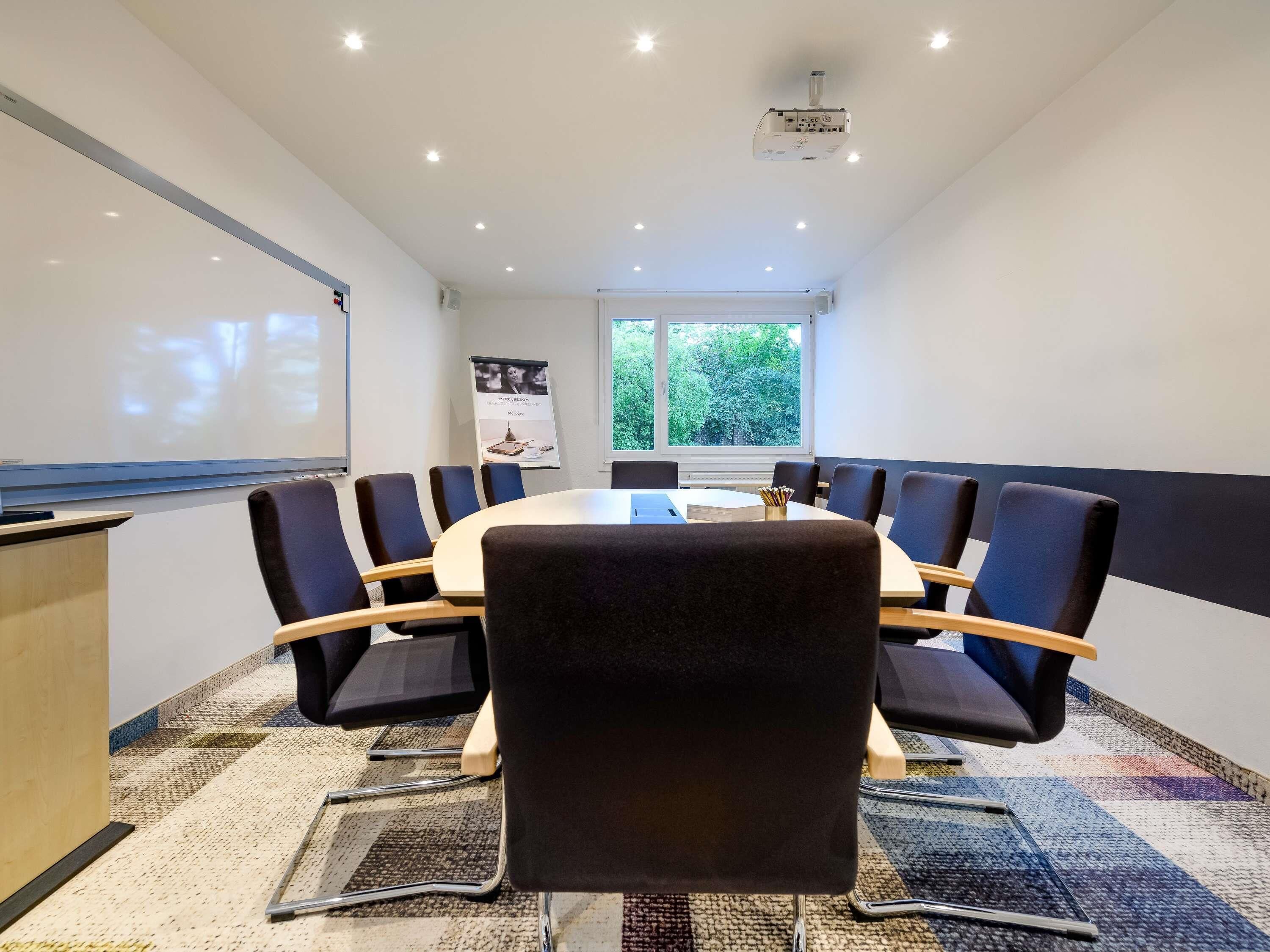 A conference room with a round table, chairs, a projector, and a whiteboard.