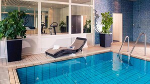 A modern indoor swimming pool with clear blue tiles, a lounge chair, and potted plants. - Mercure Hotel Köln West (Cologne)