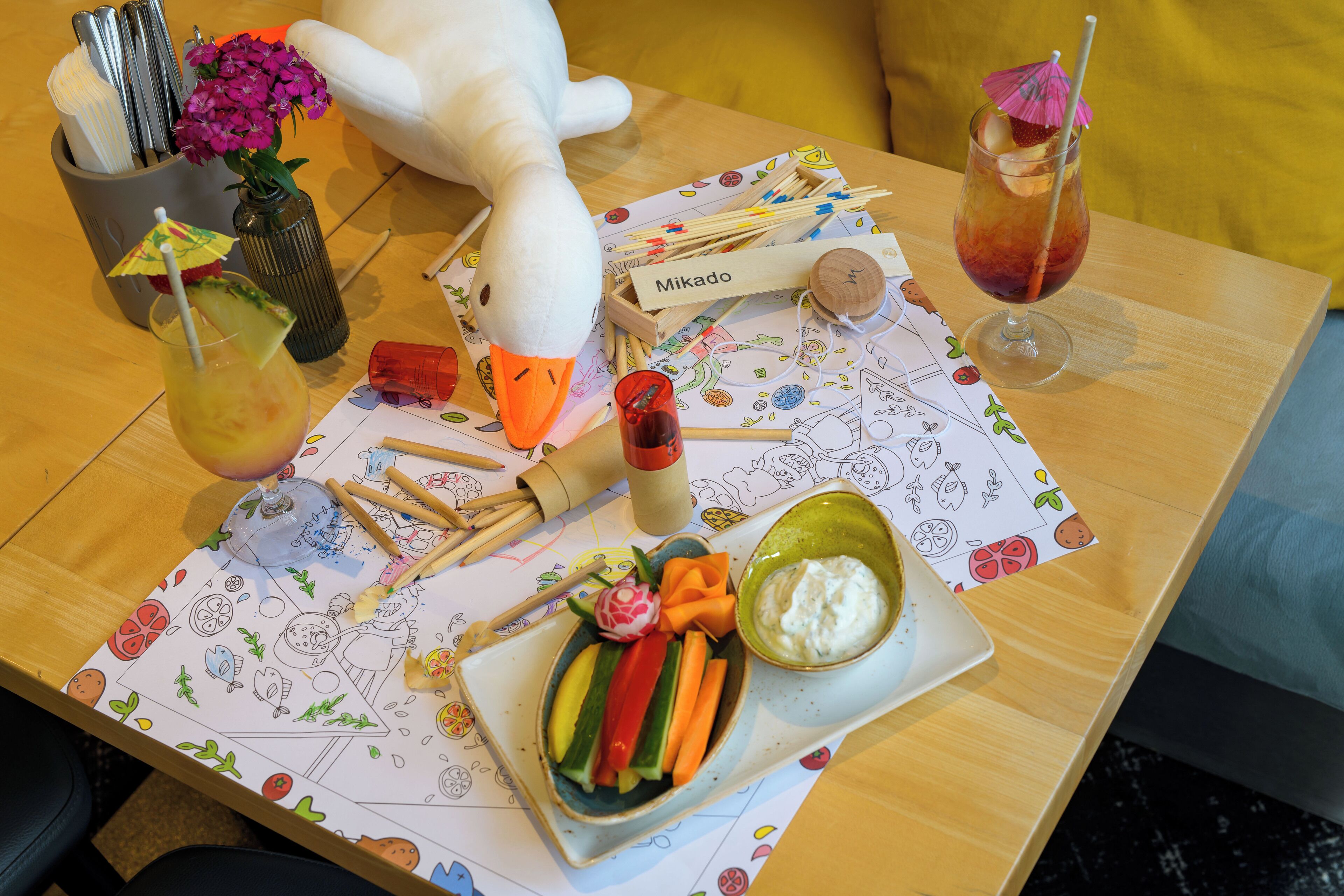 A table with a plush toy, a drink, a bowl of dip, and a plate of vegetables.