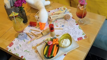 A table with a plush toy, a drink, a bowl of dip, and a plate of vegetables.