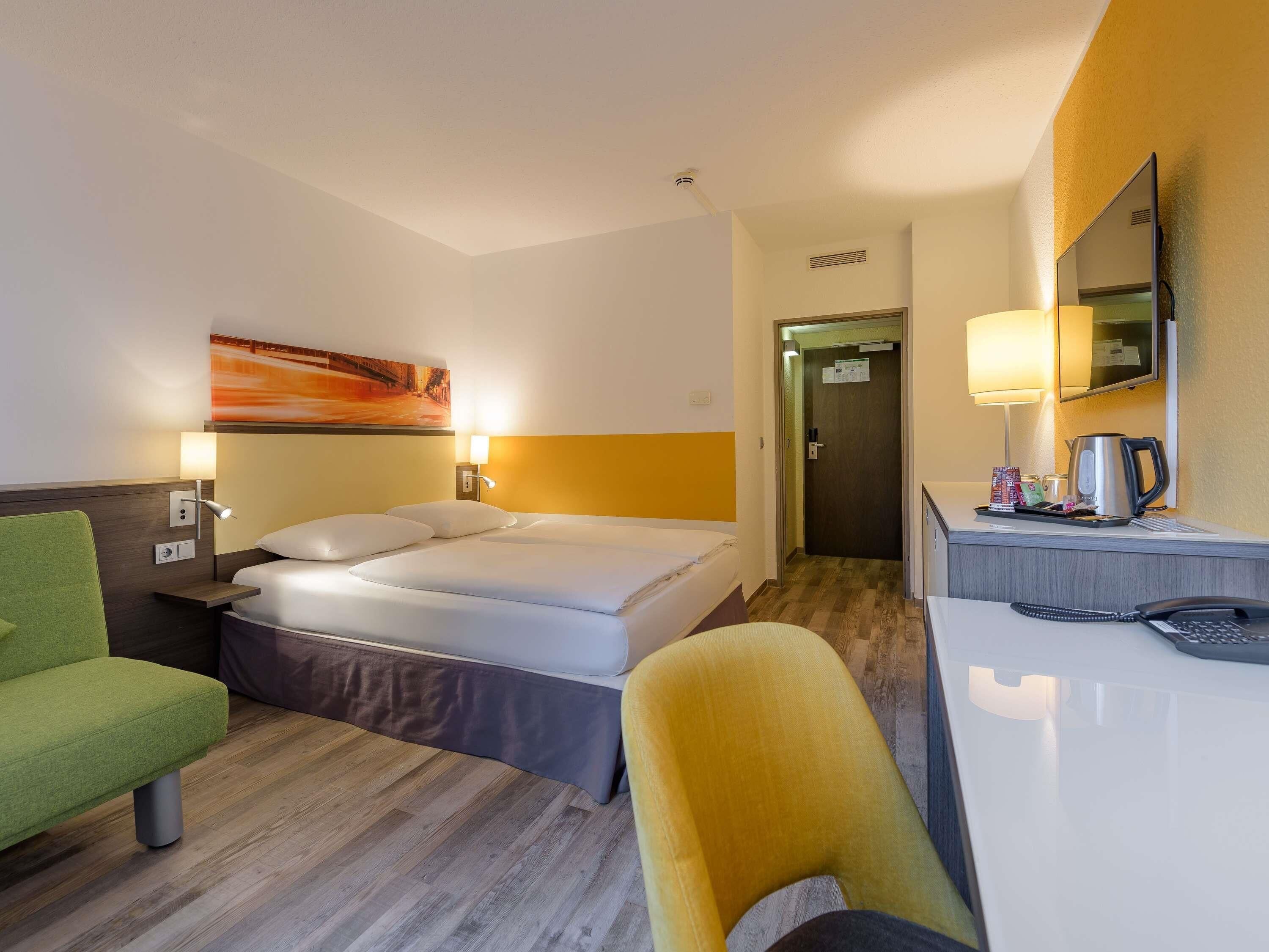A hotel room with a bed, a desk, a chair, a lamp, and a painting on the wall.