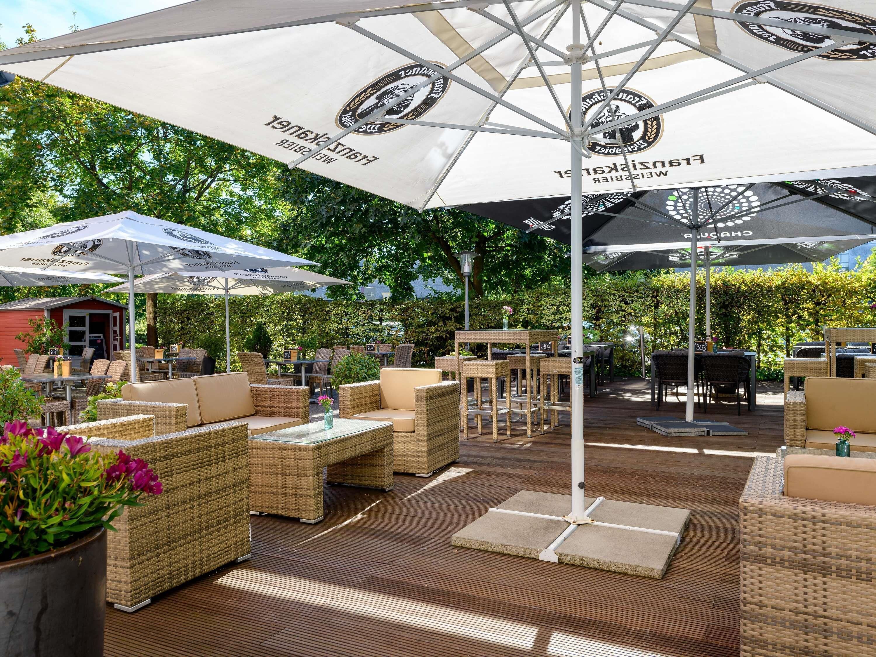 An outdoor seating area with wicker furniture and umbrellas, surrounded by greenery.
