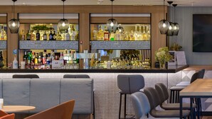 A bar area with a tiled backsplash, multiple liquor bottles, and hanging pendant lights. - Mercure Hotel Köln West (Cologne)
