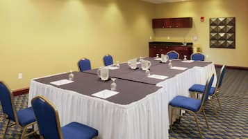 Une salle de conférence avec une longue table, des chaises bleues et un coin cuisine à l’arrière-plan.