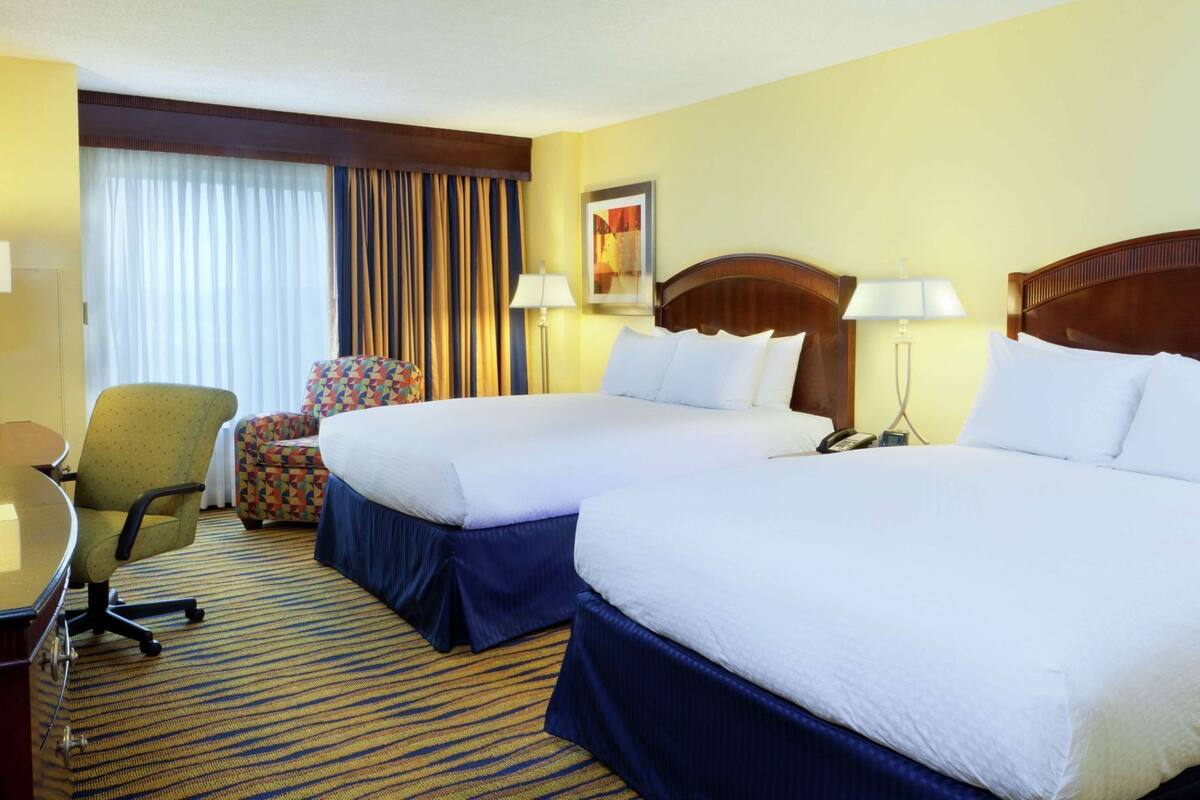 A hotel room with two beds, a desk, a chair, and a window with curtains.