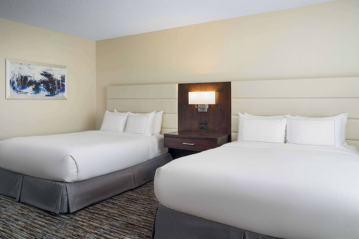 A hotel room with two beds, a nightstand with a lamp, and a painting on the wall.