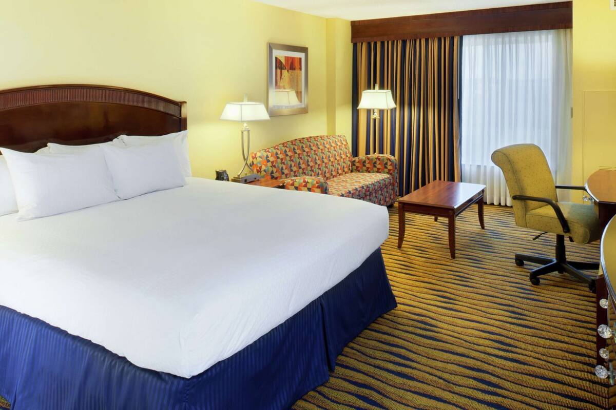 A hotel room with a large bed, a sofa, a desk, and a chair.
