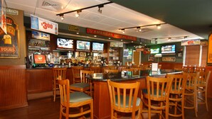 A bar with wooden chairs, a counter, and multiple televisions displaying sports. - DoubleTree by Hilton Greensboro (Greensboro)
