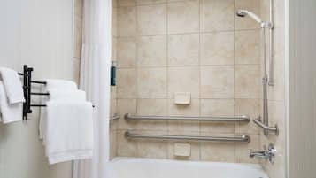 A bathroom with a bathtub, grab bars, a showerhead, and a towel rack with towels.