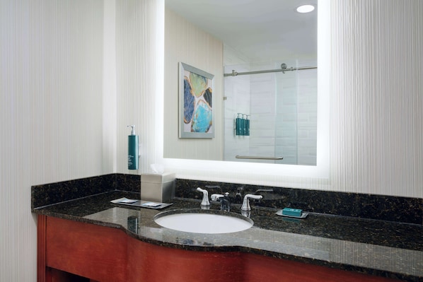 Un baño con lavamanos de mármol, dos grifos, un espejo grande y una ducha que se ve en el reflejo.