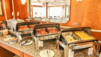 Un bufé con diversas opciones de comida, incluyendo carnes y huevos, y un espejo que refleja la sala.
