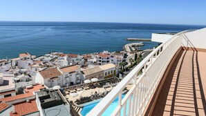 Un pueblo costero con vista al mar, un área de piscina y edificios con tejados rojos.