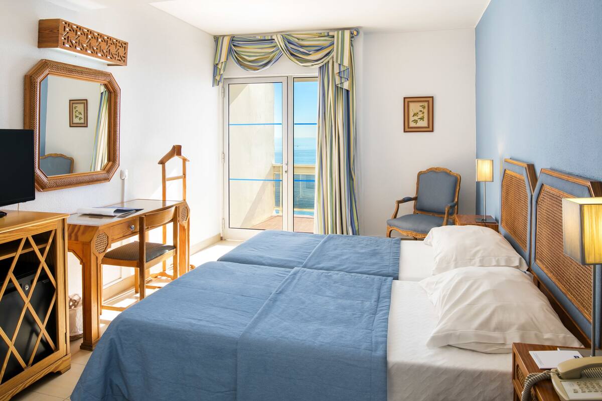 Habitació d'hotel amb llit, escriptori, cadira i vista al mar per una porta corredissa.